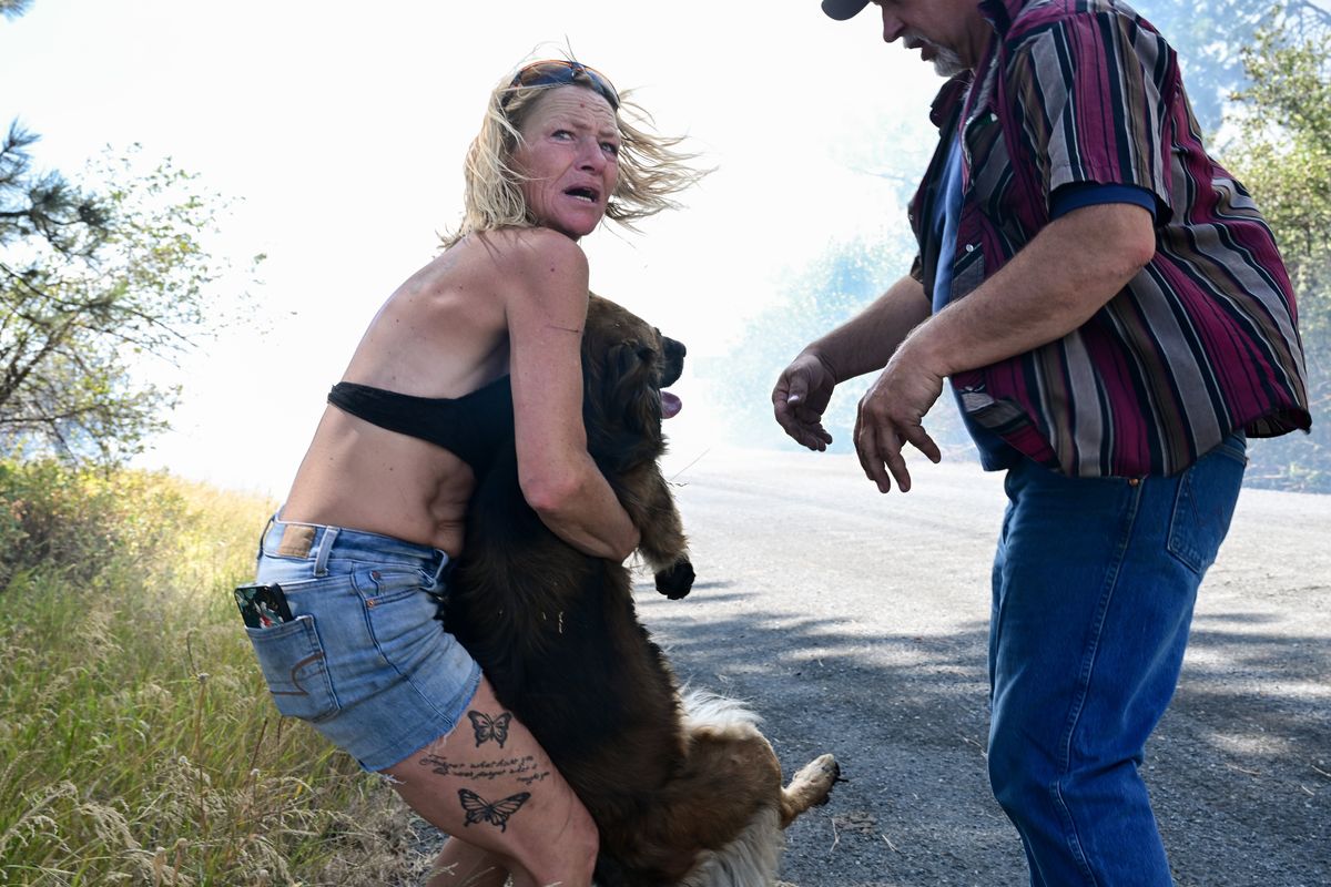 Bobbi Atwood carries her dog Luna with help from a friend after her home on West Euclid Road burned on Saturday in Spokane. Luna escaped the fire with burned paws, but Atwood said she has several pets still missing.  (Tyler Tjomsland/The Spokesman-Review)