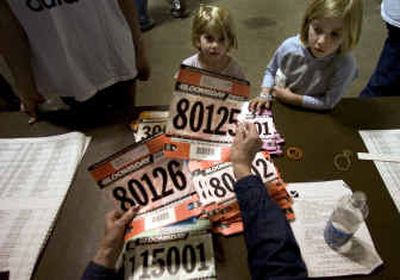 
Reagan Elzey, 4, and her sister Morgan, 6, collect their Bloomsday race numbers from volunteer Florence Haidle Friday at the Spokane Ag Trade Center.  
 (Colin Mulvany / The Spokesman-Review)