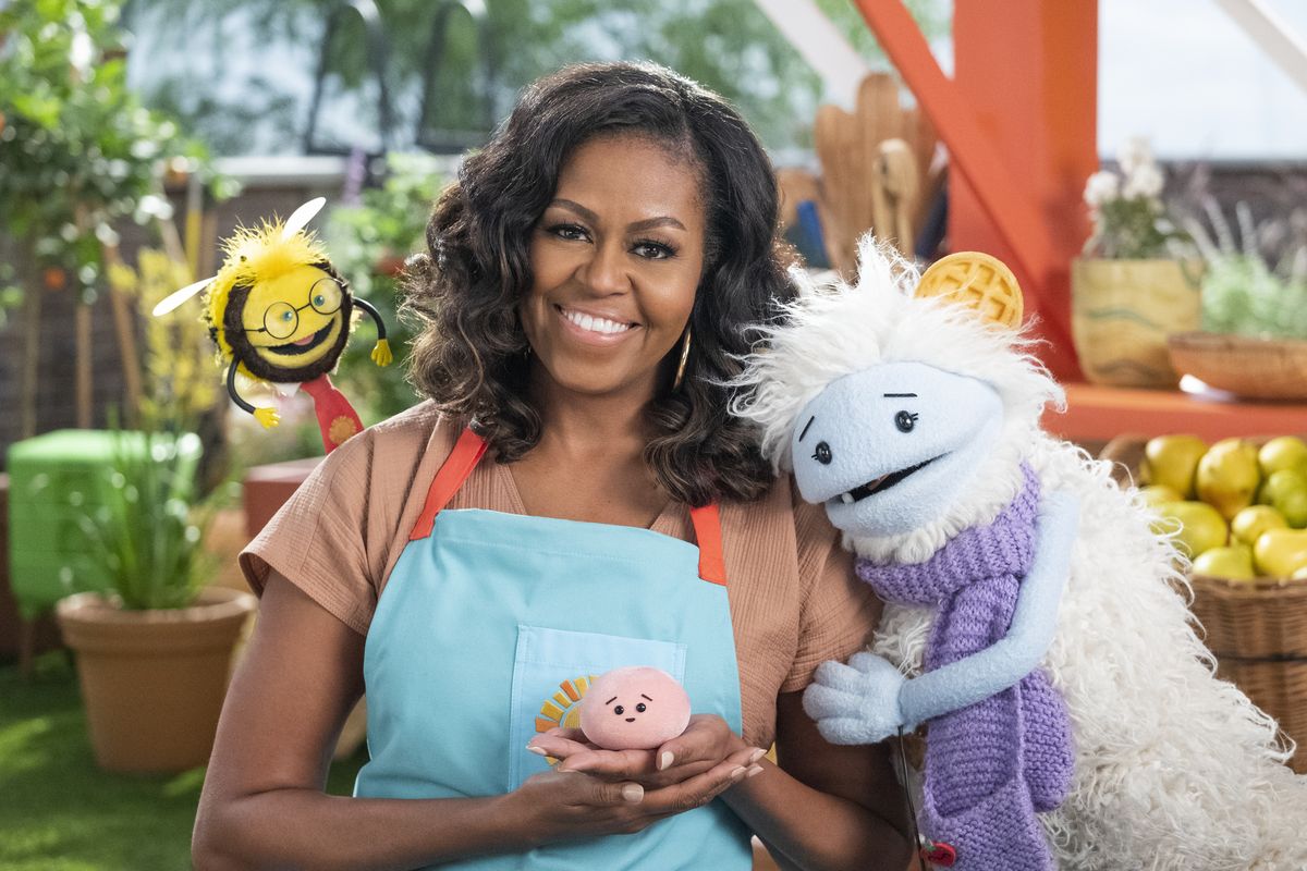 This image released by Netflix shows former first lady Michelle Obama with Busy, a bee puppet, left, Mochi, a pink round puppet, and Waffles, a furry puppet with waffle ears on the set of the children