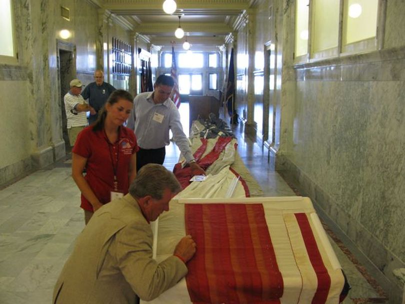 Idaho Gov. Butch Otter takes a stitch on the Idaho patch to the National 9/11 Flag, a flag that was destroyed in the collapse of the World Trade Center and is being restored with patches from each of the 50 states. It was in the Idaho state Capitol on Monday. (Betsy Russell)