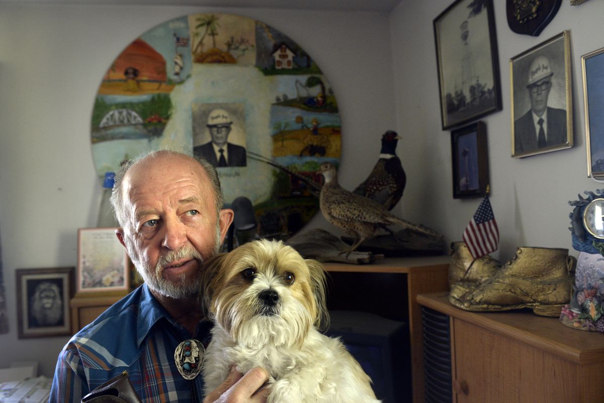 Flagpole painter Warren Hinrichs, 73, holds his dog Stitch and rests up at home in Spokane on Wednesday. He started climbing and painting flagpoles and water towers more than 50 years ago with his dad, Bill Hinrichs, seen in many photos in his home office. (Jesse Tinsley)