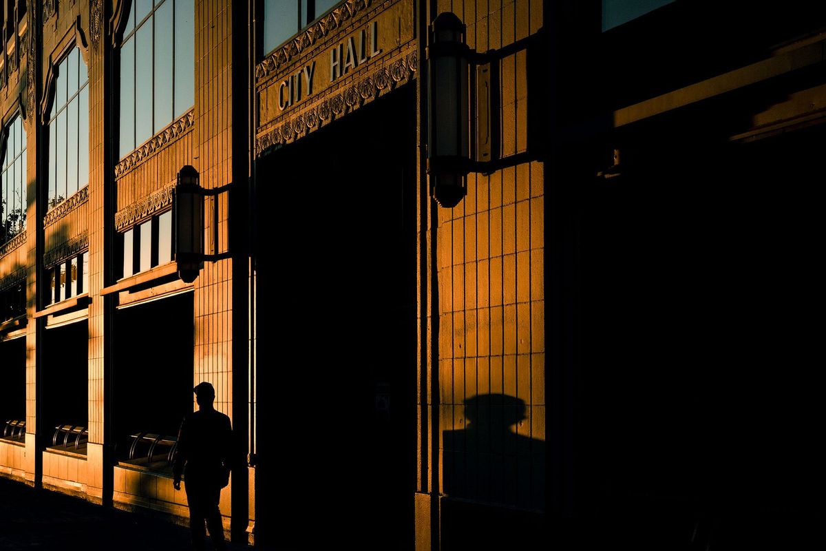 As the sun sets in downtown Spokane, Washington, a pedestrian walks by the entrance of the City Hall building, Monday, Oct 11, 2021.  (COLIN MULVANY/THE SPOKESMAN-REVIEW)