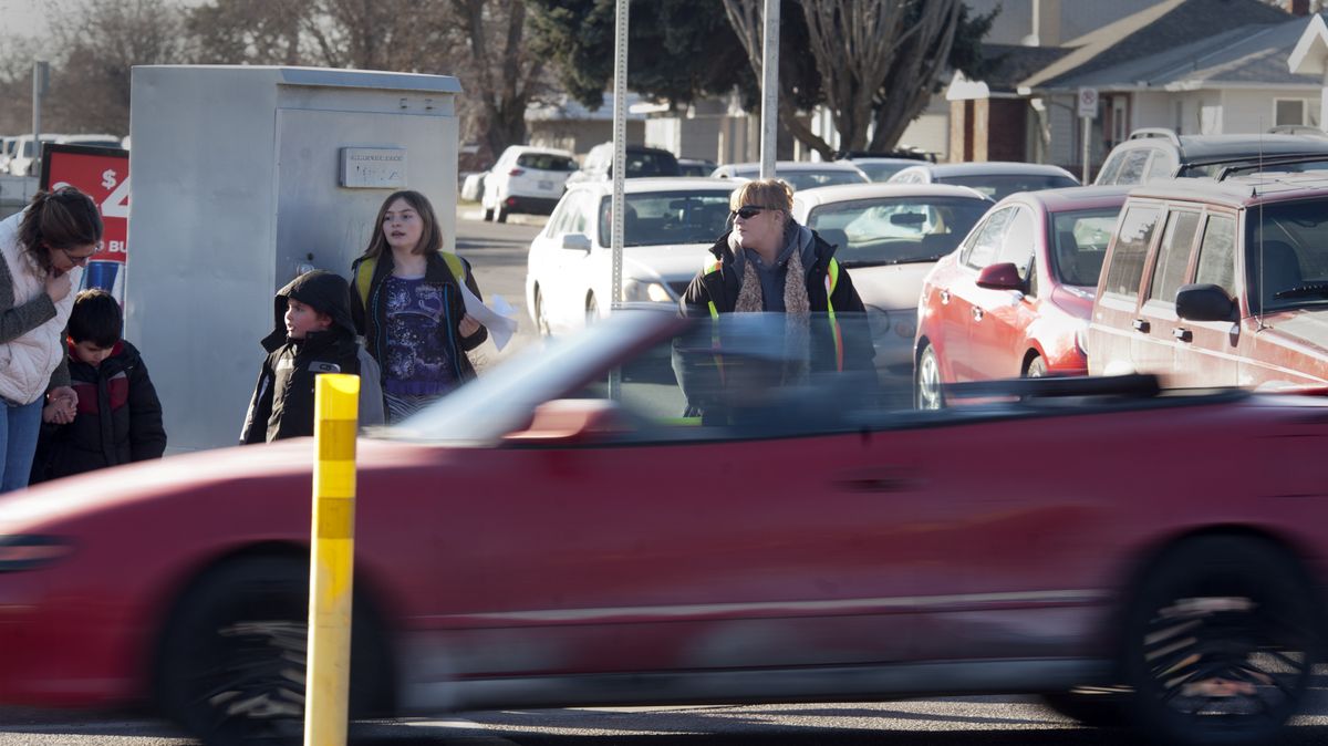 Crossing guard Jessica Martin, right, waits for the lights to change before helping Longfellow Elementary students cross Nevada Street at Empire Avenue in Spokane on Tuesday. The busy school crossing is one of the places the city of Spokane may place a speed camera to ticket those going over 20 mph during the times students are present before and after school. (Jesse Tinsley)