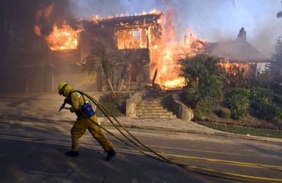 A firefighter drags a hose uphill as his crew prepares to put out a wildfire burning homes in Yorba Linda, Calif., on Saturday.  (Associated Press / The Spokesman-Review)
