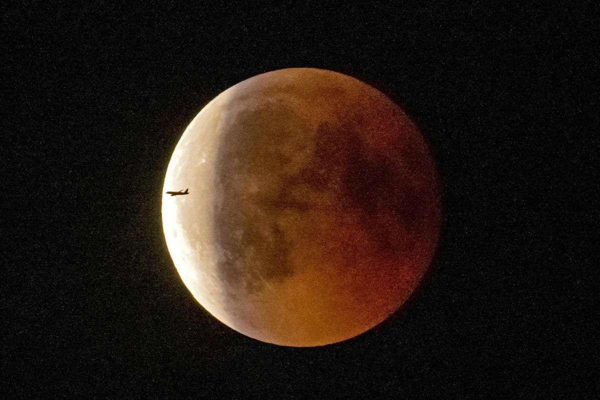 An airplane passes the blood moon immediately after the total lunar eclipse in Erfurt, Germany, Friday, July 27, 2018. Skywatchers around much of the world are looking forward to a complete lunar eclipse that will be the longest this century. (Jens Meyer / Associated Press)