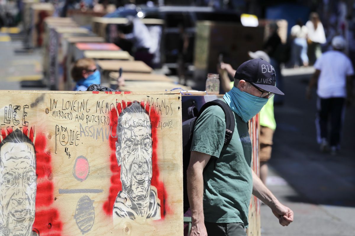 A man walks between barricades blocking a street adjacent to a closed police precinct Thursday, June 18, 2020, in Seattle, in what has been named the Capitol Hill Occupied Protest zone. Police pulled back from several blocks of the city
