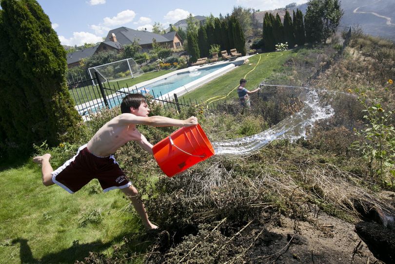 11 year old Andrew Fritz dumps a bucket of water on a smoldering area behind his house located on W. Falcon Crest Court during a fire in the foothills of Boise Thursday. Wildfire season accelerated in Idaho on Thursday as evacuations were ordered in the northern part of the state and a massive fire straddling the Idaho-Oregon border grew to 340 square miles. (Kyle Green/Idaho Statesman via AP)