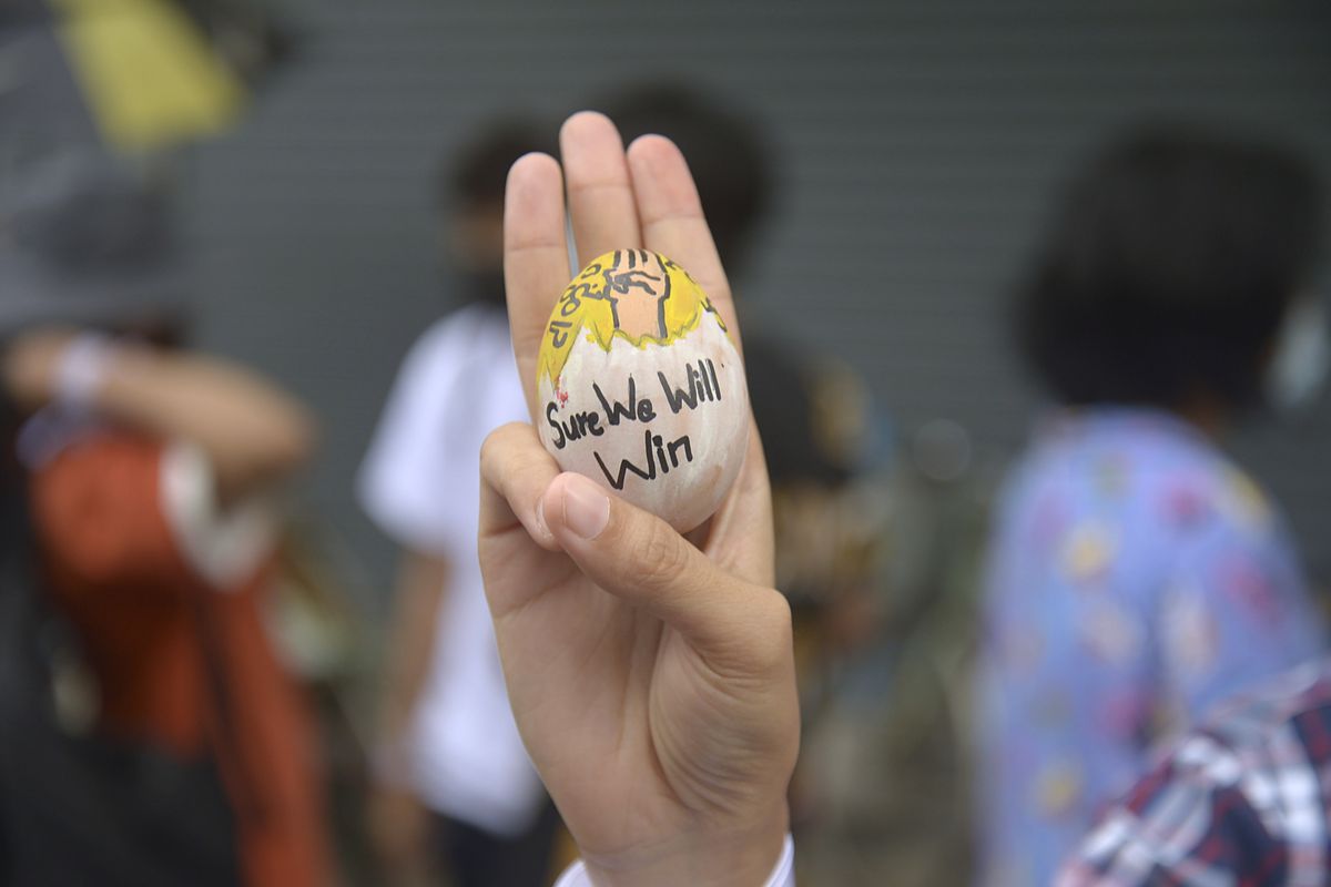 An anti-coup protester raises a decorated Easter egg along with the three-fingered symbol of resistance during a protest against the military coup on Easter Sunday, April 4, 2021, in Yangon, Myanmar. (STR)