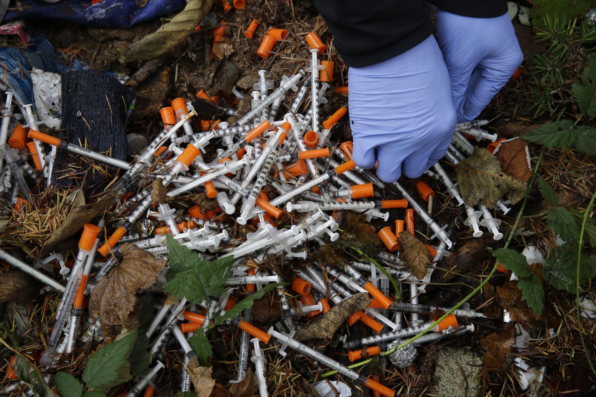 In this Nov. 8, 2017 photo, Steph Gaspar, a volunteer outreach worker with The Hand Up Project, an addiction and homeless advocacy group, cleans up needles used for drug injection that were found at a homeless encampment in Everett, Wash. (Ted S. Warren / Associated Press)