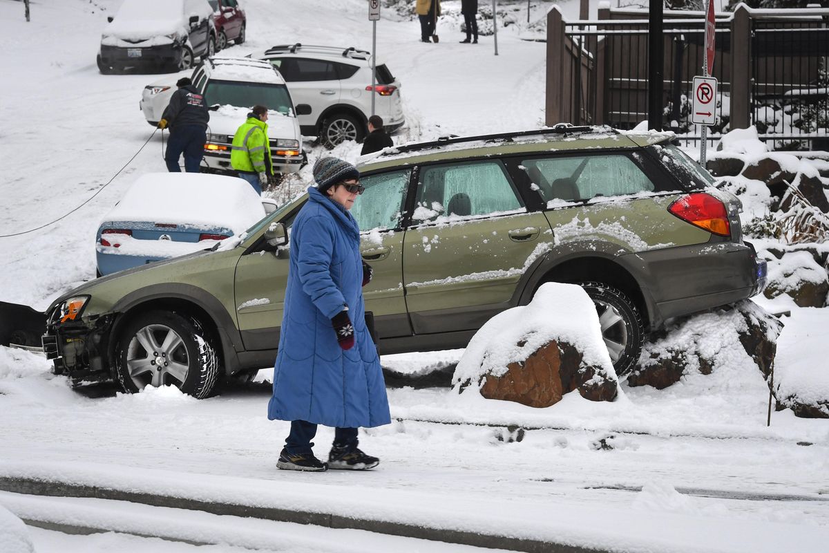 A pedestrian walks cautiously through a new snowfall as towing crews clean up a tangle of cars at the corner of Lincoln Street and Seventh Avenue, Wednesday morning Dec. 11, 2019, in Spokane, Wash. (Dan Pelle / The Spokesman-Review)