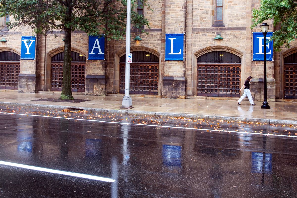 A woman walks by a Yale sign reflected in the rainwater in the street on Aug. 22 on the Yale University campus in New Haven, Conn.  (Ted Shaffrey)