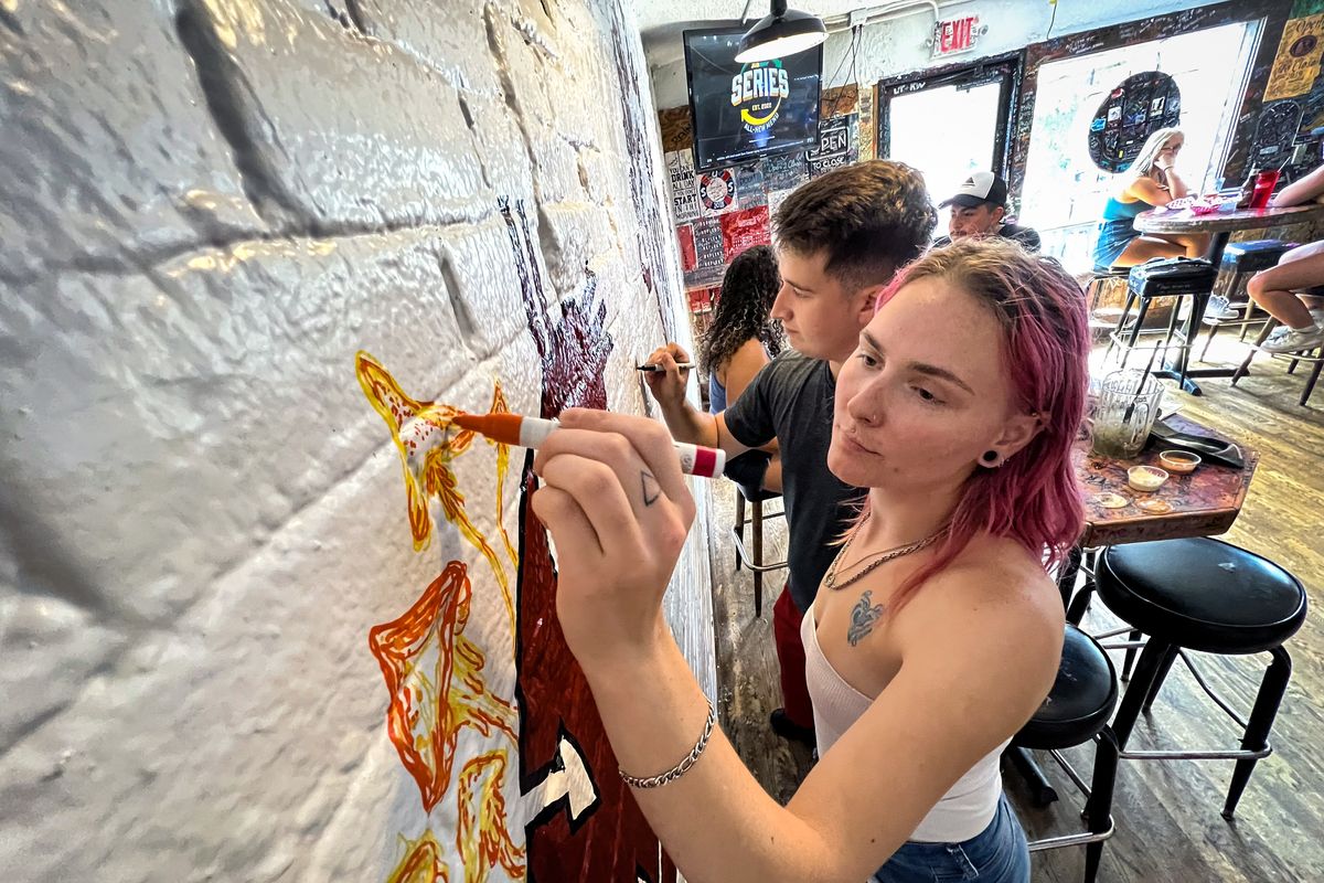 Freshly painted, Ciera Parker and Jackson Dorsett draw on the Coug Wall, a 90-year tradition for the historic restaurant in Pullman. The Coug reopened for business August 10, 2022, as WSU students begin to arrive back on campus.  (COLIN MULVANY/THE SPOKESMAN-REVIEW)