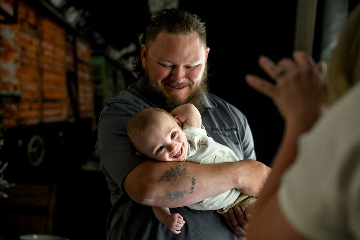 Kane Nash’s dad, Chris, holds him while his mom, Amber, gets him to smile for the camera at their home in Blanchard, Idaho, on Wednesday, July 3, 2024. Kane was born at 23 weeks at Providence Sacred Heart, weighing just 15 ounces on July 9, 2023.  (Kathy Plonka/The Spokesman-Review)