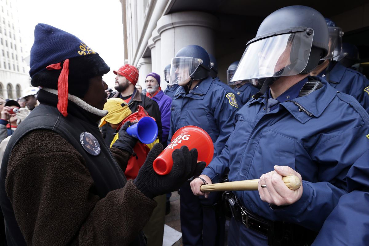 A protester rallies in front of Michigan State Police at the George W. Romney State Building, where Gov. Snyder has an office in Lansing, Mich., Tuesday, Dec. 11, 2012. The crowd is protesting right-to-work legislation passed last week. Michigan could become the 24th state with a right-to-work law next week. Rules required a five-day wait before the House and Senate vote on each other's bills; lawmakers are scheduled to reconvene Tuesday and Gov. Snyder has pledged to sign the bills into law. (Paul Sancya / Associated Press)