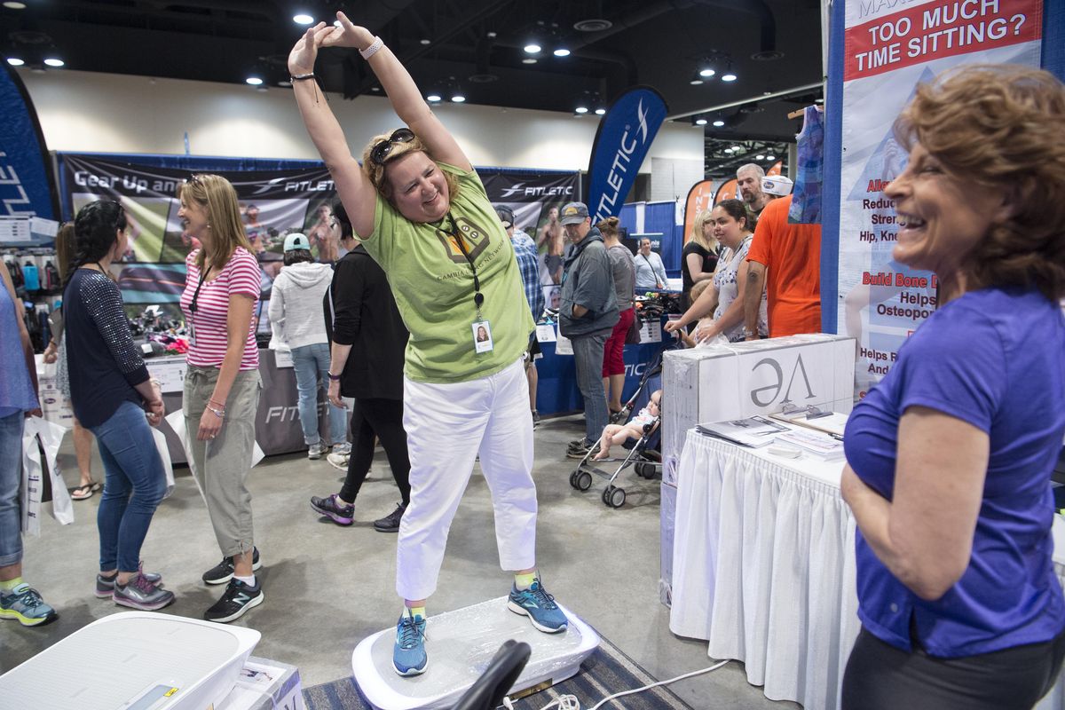 Kimberly Thielman, left, tries out the MaxBurn, a motorized oscillating platform designed to work and massage muscles, according to salesperson Melody Creevey, right, at the Bloomsday, May 4, 2018 at the Spokane Convention Center. (Jesse Tinsley / The Spokesman-Review)