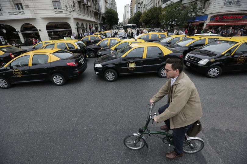 A man rides his bicycle past taxis blocking a main avenue in Buenos Aires, Argentina, Tuesday, April 12, 2016. Hundreds of taxi drivers paralyzed parts of the capital during rush hour to protest Uber launching its service on Tuesday in defiance of local authorities. (AP Photo/Victor R. Caivano)