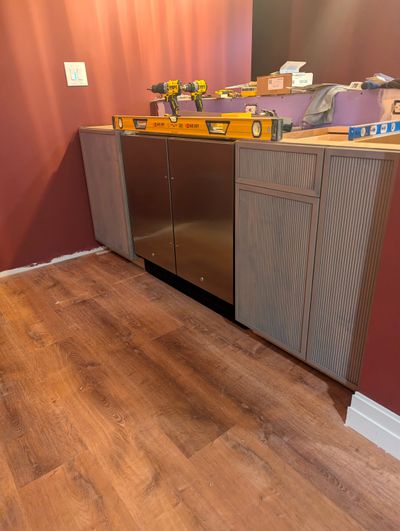 There are three cabinets in this photo. A sink base is to the left of the refrigerator/freezer. A trash-can cabinet and small slide-out shelf cabinet are to the right. This is the bar area of a basement speakeasy.  (Tribune Content Agency)