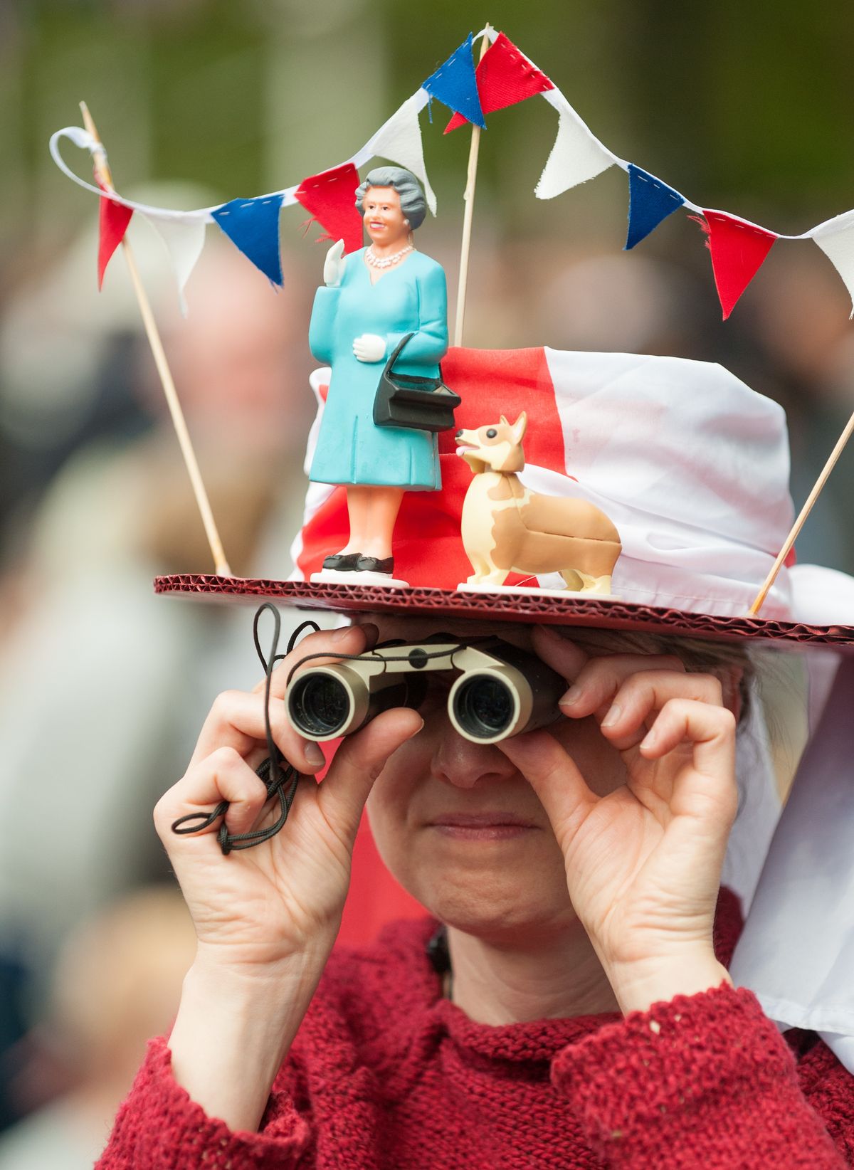 A woman in a fancy dress hat featuring Queen Elizabeth II and a corgi waits for the start of the Diamond Jubilee concert in London on Monday. (Associated Press)