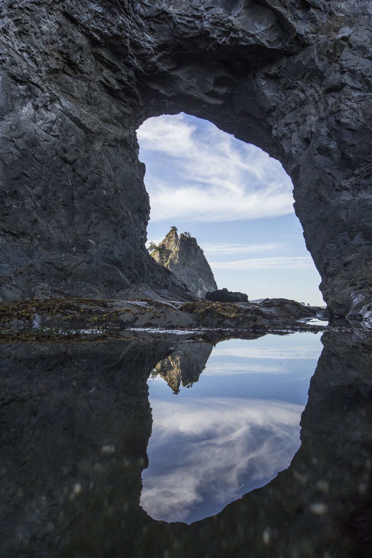 Hole in the Wall, shown here reflected in a tide pool, is a popular destination at Olympic National Park’s Rialto Beach. (STEVE RINGMAN)