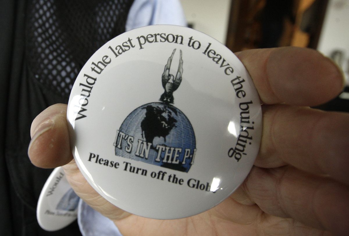 A Seattle Post-Intelligencer worker holds out a badge being distributed among employees Monday in Seattle advising the last person in the building to “Please Turn off the Globe.” (Elaine Thompson / The Spokesman-Review)