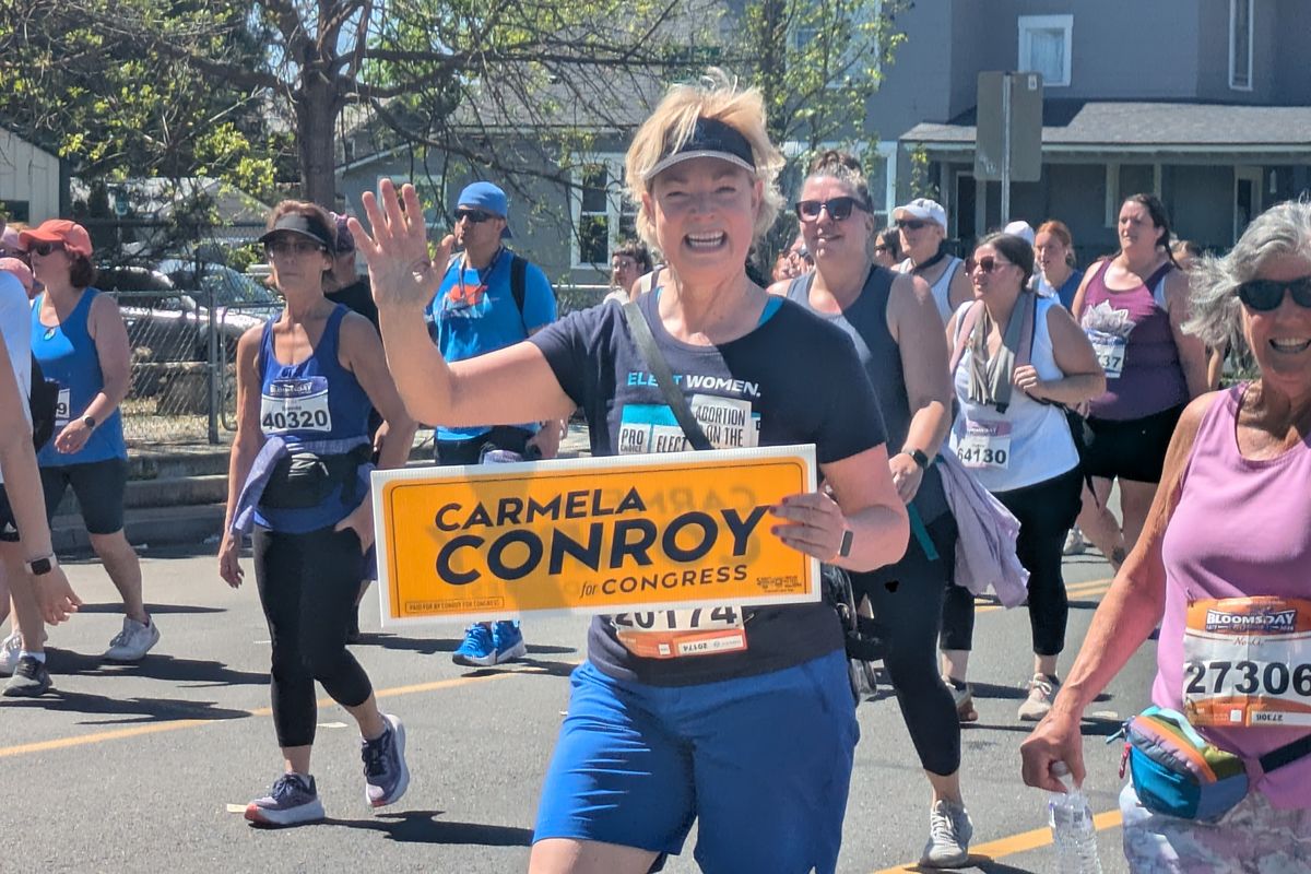 Congressional candidate Carmela Conroy holds up a campaign sign and waves as she walks the last mile of Bloomsday. (Emry Dinman/The Spokesman-Review )