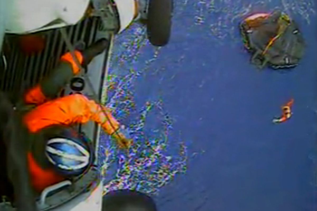 In this image made from video and released by the U.S. Coast Guard, a USCG rescue swimmer, in water at right, and a crew member use a hoist to bring up a survivors into a helicopter. A replica tall ship caught in Hurricane Sandy