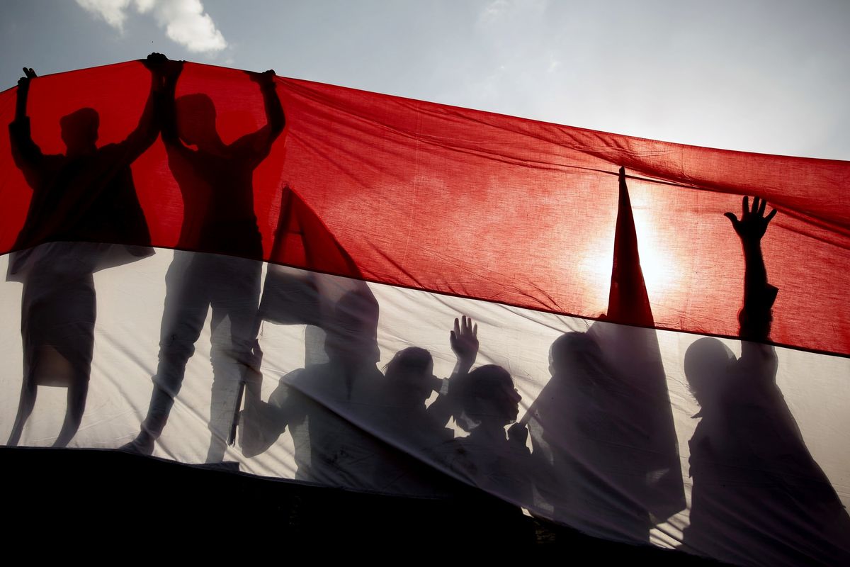 FILE - In this Sept. 26, 2016 file photo, men are silhouetted against a large representation of the Yemeni flag as they attend a ceremony to mark the anniversary of North Yemen