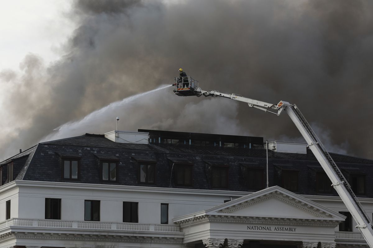 Firefighters, atop a hoist, fight the re-ignited fire at Parliament in Cape Town, South Africa, Monday, Jan 3, 2022. Firefighters are again on the scene after a major blaze tore through the precinct a day earlier.  (Nardus Engelbrecht)