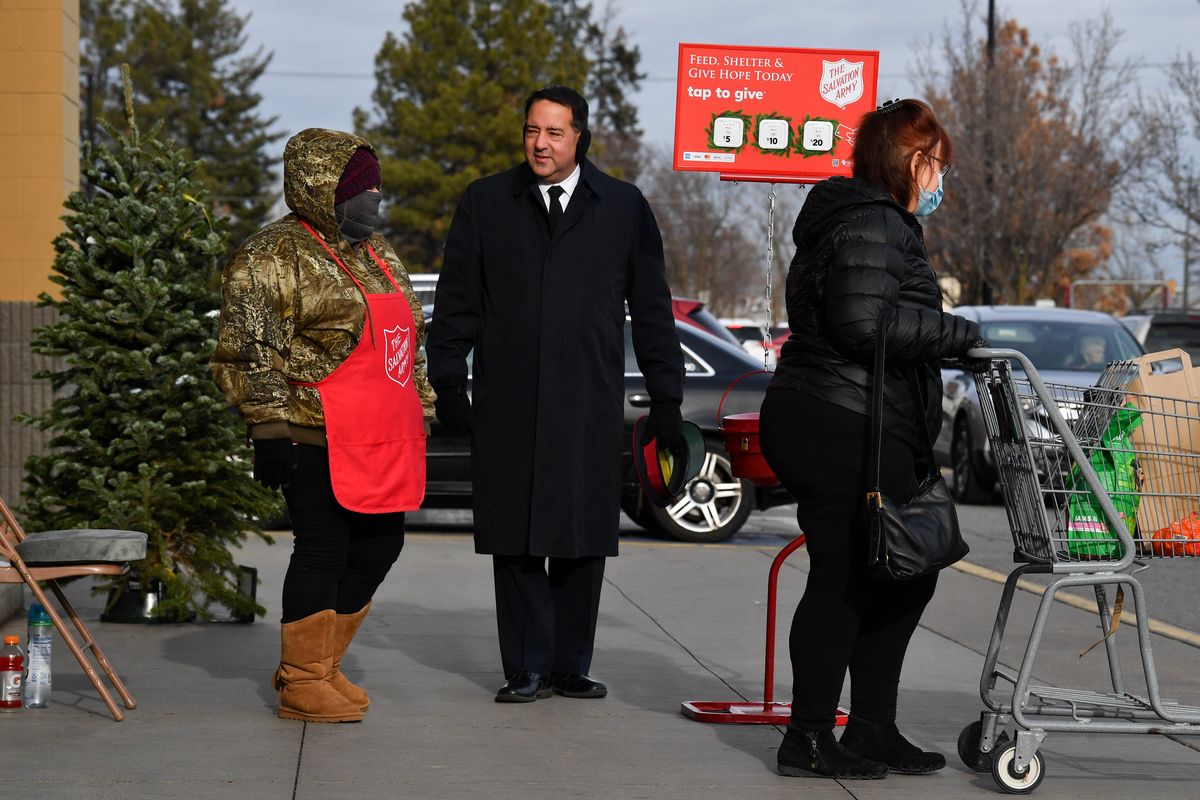 Major Ken Perine of The Salvation Army of Spokane, center chats with bell ringer Mechele Gates-Engle, left, as shoppers pass on Wednesday, Dec 15, 2021, in Spokane, Wash.  (Tyler Tjomsland/The Spokesman-Review)