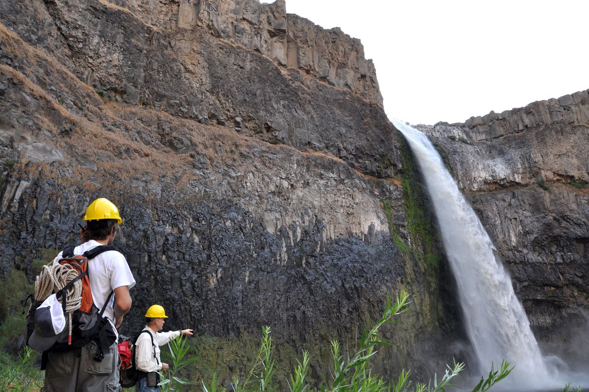 Whitman College geology student Curtis Reid, left, observes with professor Bob Carson as students anchored with climbing gear at the top of the rim lower a tape to measure the height of Palouse Falls. (The Spokesman-Review)