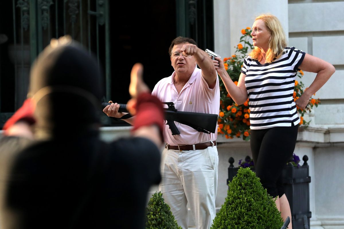 FILE - In this June 28, 2020 file photo, armed homeowners Mark and Patricia McCloskey, standing in front their house along Portland Place confront protesters marching to St. Louis Mayor Lyda Krewson