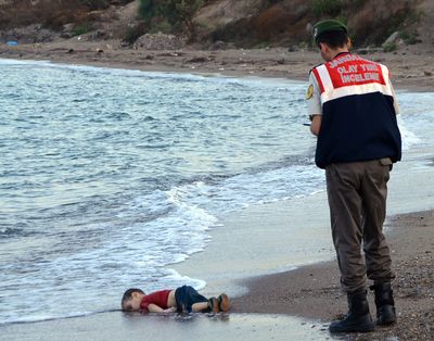 A police officer investigates before carrying the body of Aylan Kurdi, 3, near Bodrum, Turkey, on Wednesday. His brother and mother also drowned when a boat carrying migrants capsized. (Associated Press)
