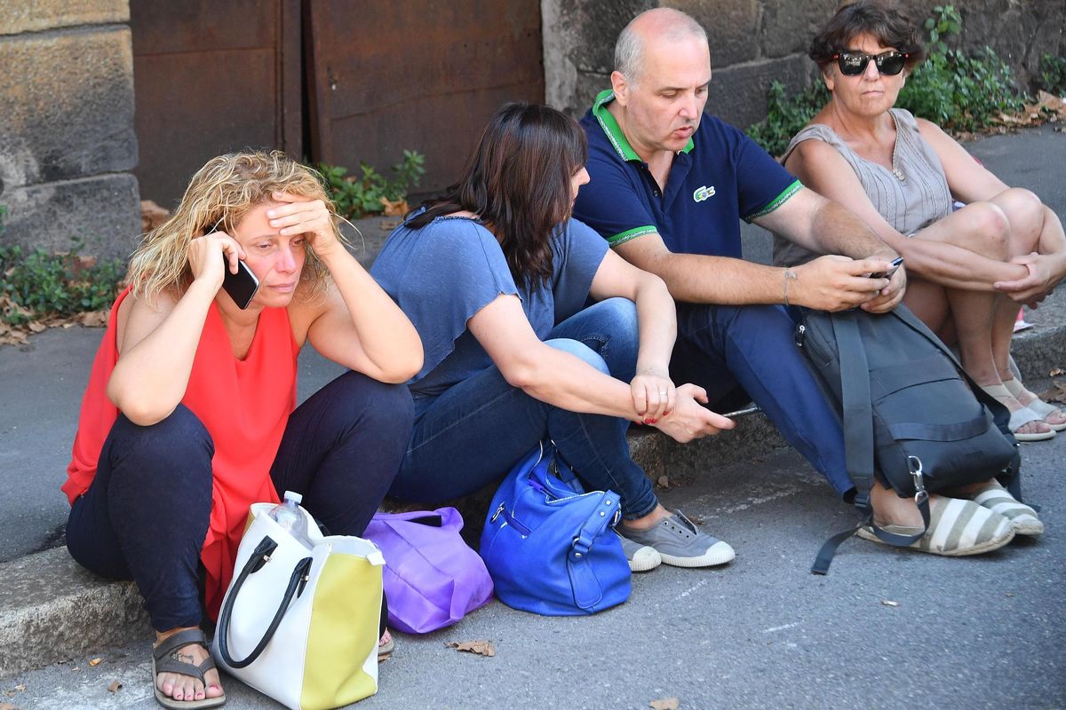 Displaced residents that where evacuated from buildings close to collapsed Morandi highway bridge, sit on the side of a street, in Genoa, northern Italy, Wednesday, Aug. 15, 2018. A bridge on a main highway linking Italy with France collapsed in the Italian port city of Genoa during a sudden, violent storm, sending vehicles plunging 90 meters (nearly 300 feet) into a heap of rubble below. (Luca Zennaro / Associated Press)