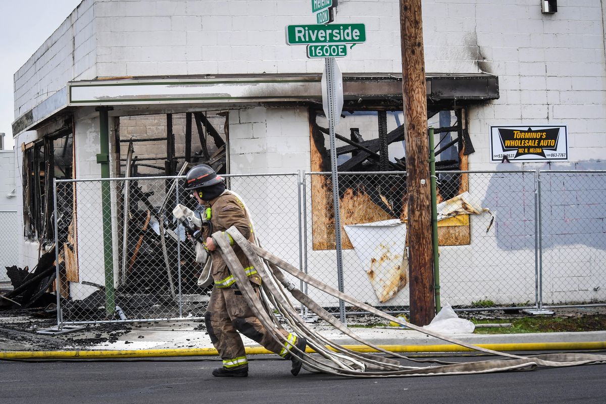 Spokane firefighter Tom Harvey hauls fire hose past the burned out Tormino’s Sash and Glass building, Wednesday, May 1, 2019, at the corner of Riverside Avenue and Helena Street. (Dan Pelle / The Spokesman-Review)