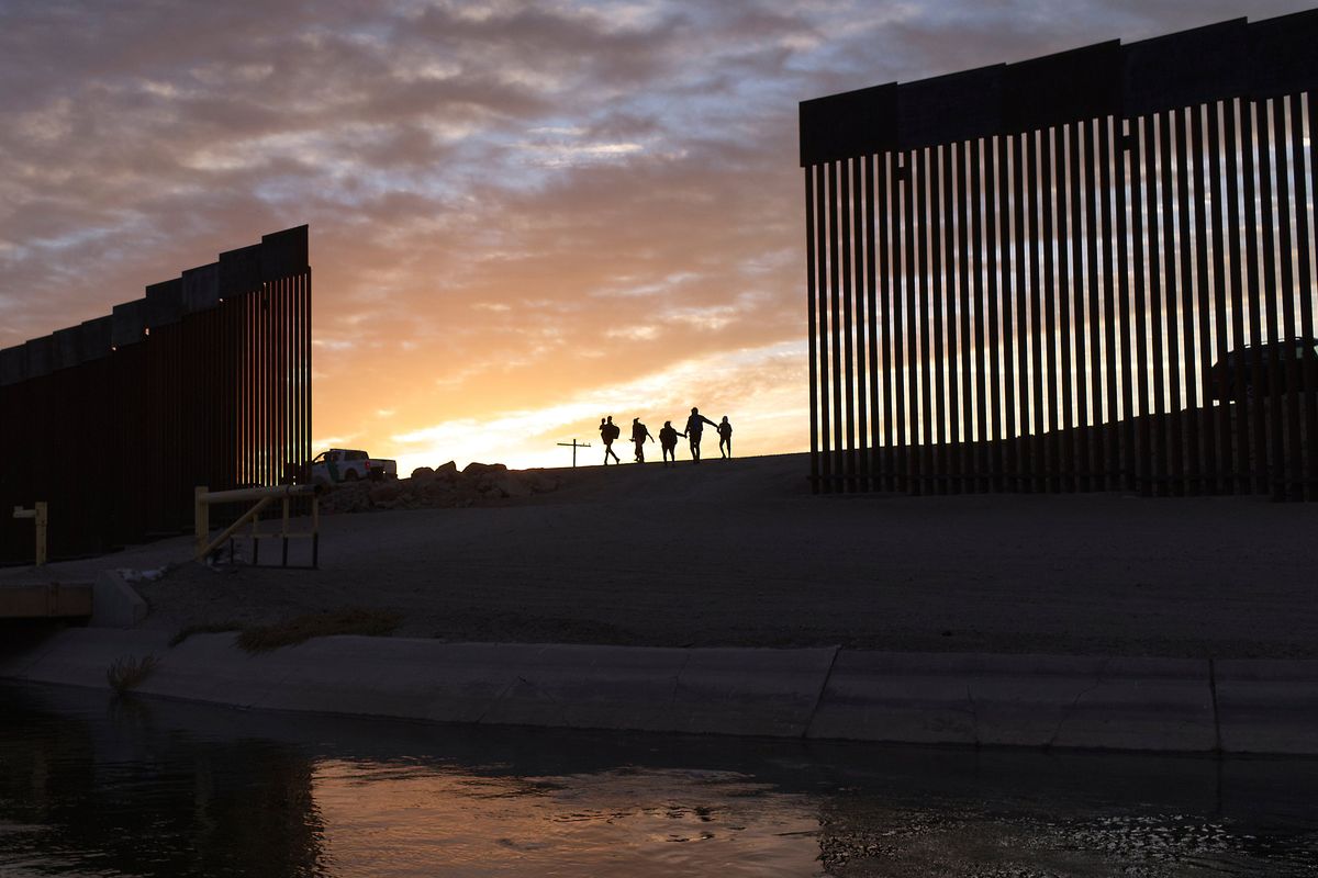 A pair of migrant families from Brazil seeking asylum walk through a gap in the border wall on June 10 to reach the United States after crossing from Mexico to Yuma, Ariz. (Eugene Garcia)