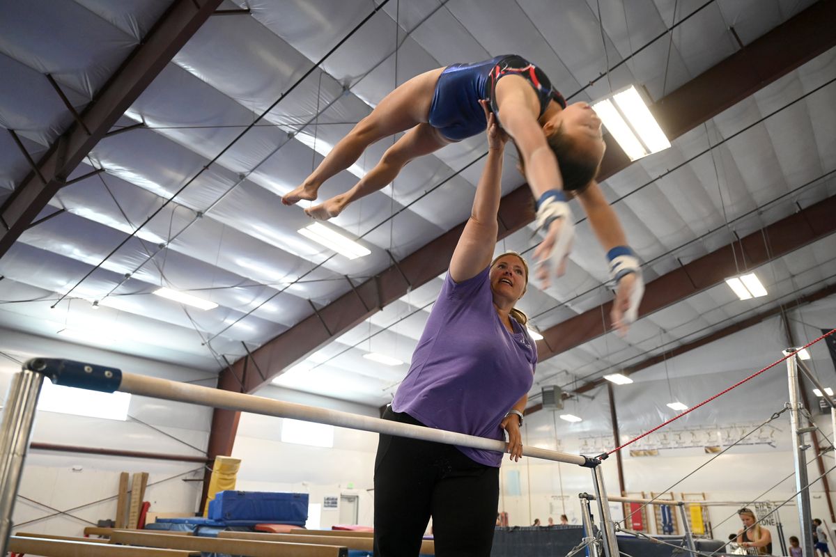 Coach Melanie Bixby spots Tianmei Dwyer, 14, while working on an uneven parallel bars routine Thursday, July 29, 2021 at Dynamic Gymnastics in north Spokane.  (Jesse Tinsley/THE SPOKESMAN-REVIEW)