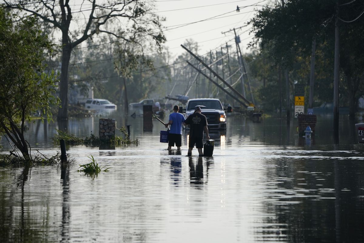 People walk up a street flooded in the aftermath of Hurricane Ida, Wednesday, Sept. 1, 2021, in Jean Lafitte, La. Louisiana residents still reeling from flooding and damage caused by Hurricane Ida are scrambling for food, gas, water and relief from the oppressive heat.  (John Locher)