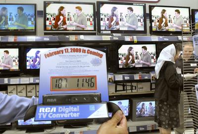 Dale Johnson, manager of Spokane’s South Regal ShopKo, holds a converter box in a display showing the countdown to the switchover to all-digital TV in February. Salesperson Windi Selle, far right, helps customer Billie Todd pick out a new TV.  (CHRISTOPHER ANDERSON / The Spokesman-Review)