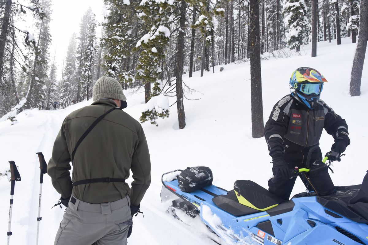 Justin Hall, left, watches as a snowmobiler passes him on a trail in the St. Regis Basin near Lookout Pass in early January. (Eli Francovich / The Spokesman-Review)