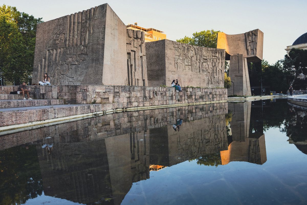 Visitors sit around “Monument to the Discovery of America,” four hulking Brutalist cast-concrete forms designed by Joaquín Vaquero Turcios, in Madrid, May 24, 2025. The forms are engraved with figures and phrases from officers, sailors and others related to Christopher Columbus’ voyage.  (New York Times)