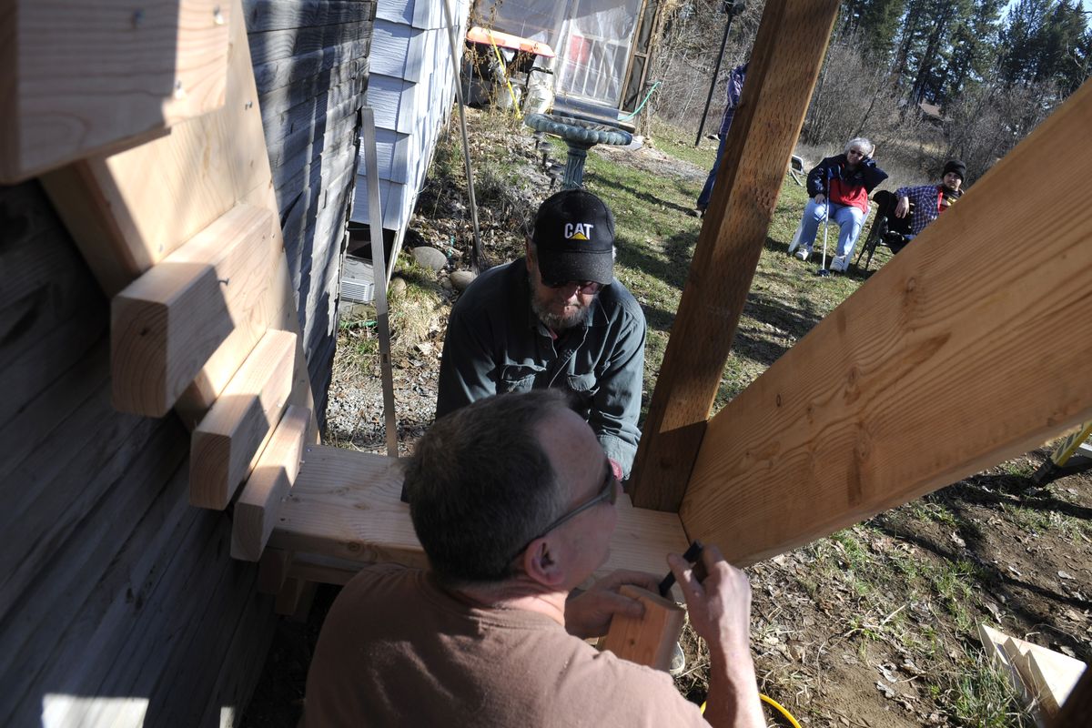 Contractor Scott Whitman, foreground, and volunteer Jerry Gordon  build a simple set of stairs on a garage building for Evelyn DeLaughter, who watches from her lawn chair with grandson Michael Jones, right,   in Priest River on Saturday. (PHOTOS BY JESSE TINSLEY)