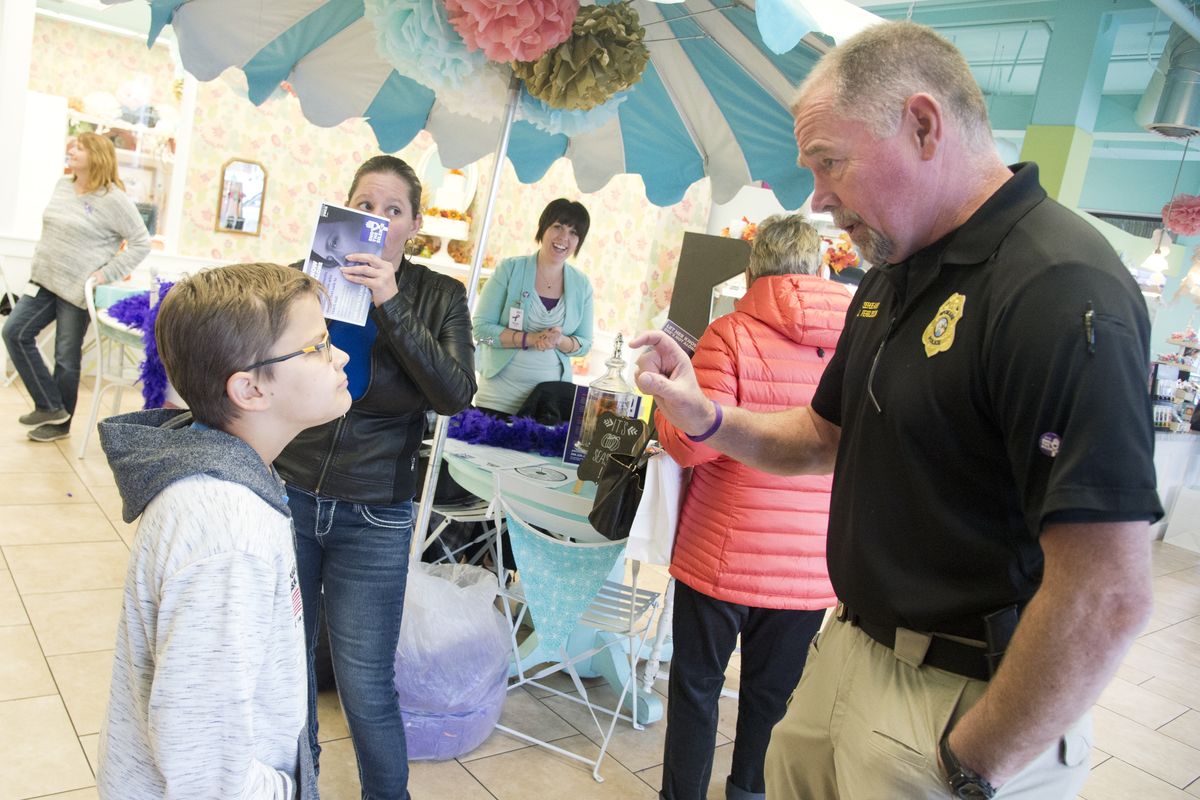 Sgt. Jordan Ferguson, right, answers a question from Kurtis Pratt, 10, left, about how Tazers work at Sweet Frostings bakery, Thursday, Oct. 20, 2016 as Ferguson and other officers were handing out free mini cupcakes and talking with patrons about domestic violence. The officers were helping the Spokane YWCA launch the "End the Silence" campaign, during National Domestic Violence Action Month. All month long, the bakery will sell large frosted cookies with the words "End the Silence" and donate $1 from each cookie to the YWCA