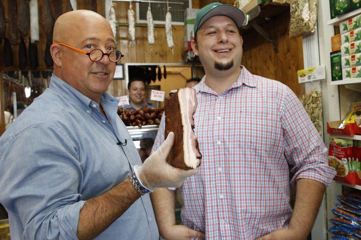 In this photo taken Thursday, July 20, 2017, "Bizarre Foods" host Andrew Zimmern, left, holds a slab of Carska bacon after savoring a small piece of it at Muncan Meats in Astoria, Queens, in New York. Marko Stefanovic, grandson of the store