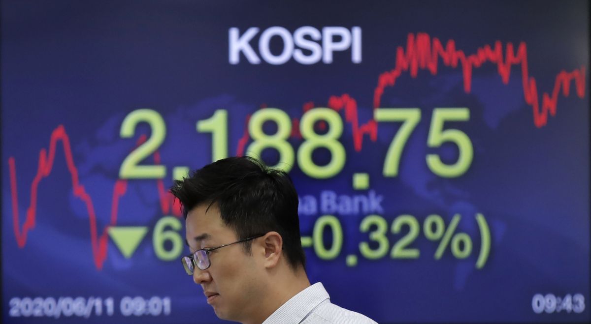 A currency trader walks by a screen showing the Korea Composite Stock Price Index (KOSPI) at the foreign exchange dealing room in Seoul, South Korea, Thursday, June 11, 2020. Asian shares were mostly lower Thursday, with Tokyo dropping more than 1% as the Japanese yen gained after the Federal Reserve said it would keep interest rates low through 2022.  (Lee Jin-man)