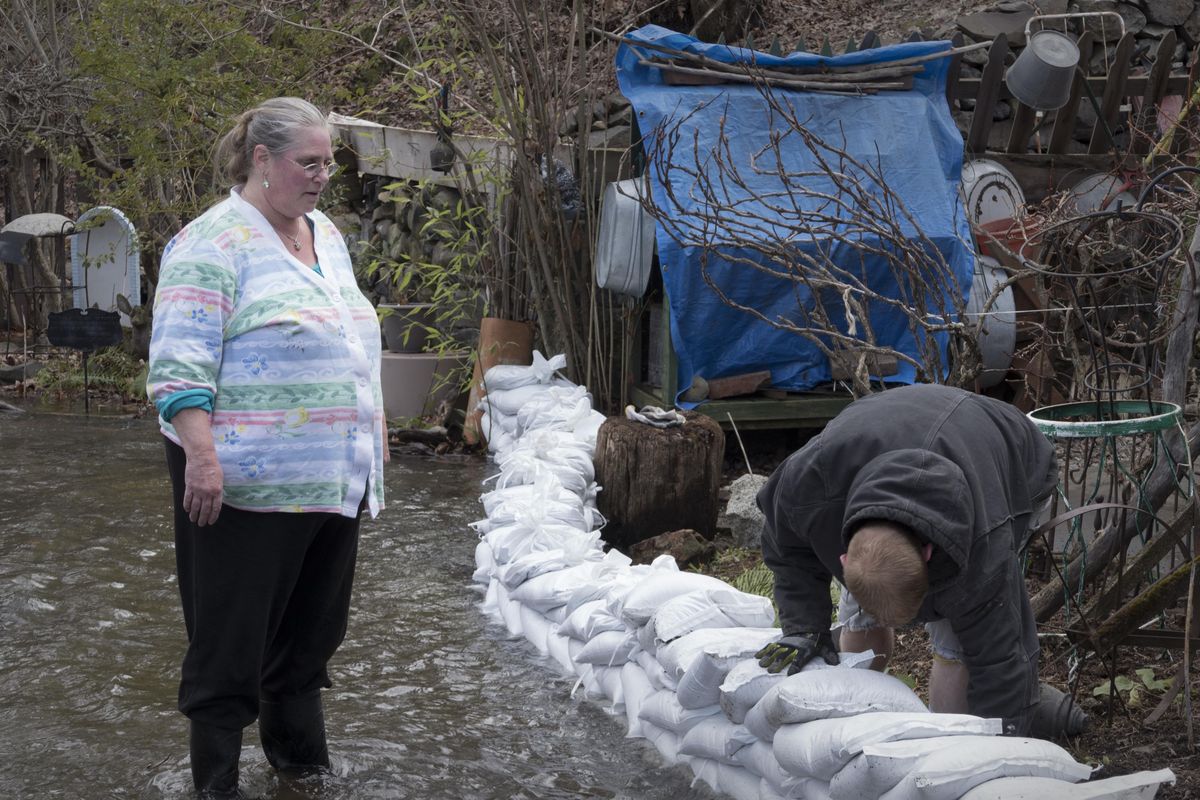 Deanna Smulan, left, watches as volunteers  help sandbag around her mother’s 1902 house, which is right on the Spokane River. (Jesse Tinsley / The Spokesman-Review)