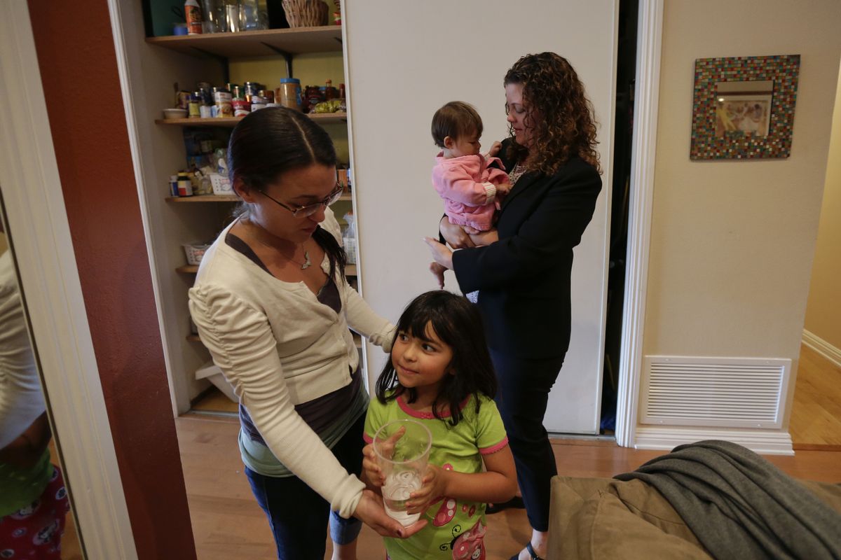 In this Sept. 26, 2012 picture, Sabina Widmann, right, holds her baby girl Stella while domestic worker Alicia Wotherspoon, left, helps her daughter Luna with a glass of water before work at their home in San Diego. (Gregory Bull / Associated Press)