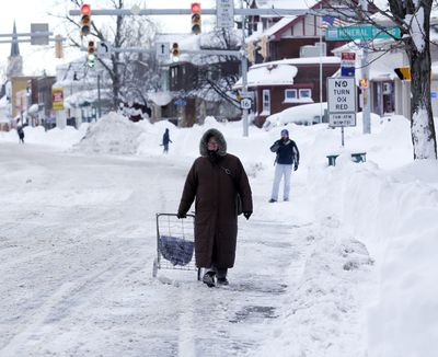 A woman walks along a street on Thursday in Buffalo, where lake-effect snow has left more than 7 feet of snow in some areas. (Associated Press)