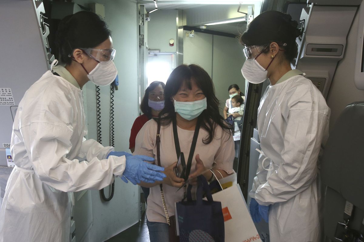 Participants are greeted by flight attendants in protective suits during a mock trip abroad at Taipei Songshan Airport in Taipei, Taiwan, Tuesday, July 7, 2020. Dozens of would-be travelers acted as passengers in an activity organized by Taiwan’s Civil Aviation Administration to raise awareness of procedures to follow when passing through customs and boarding their plane at Taipei International Airport.  (Chiang Ying-ying)