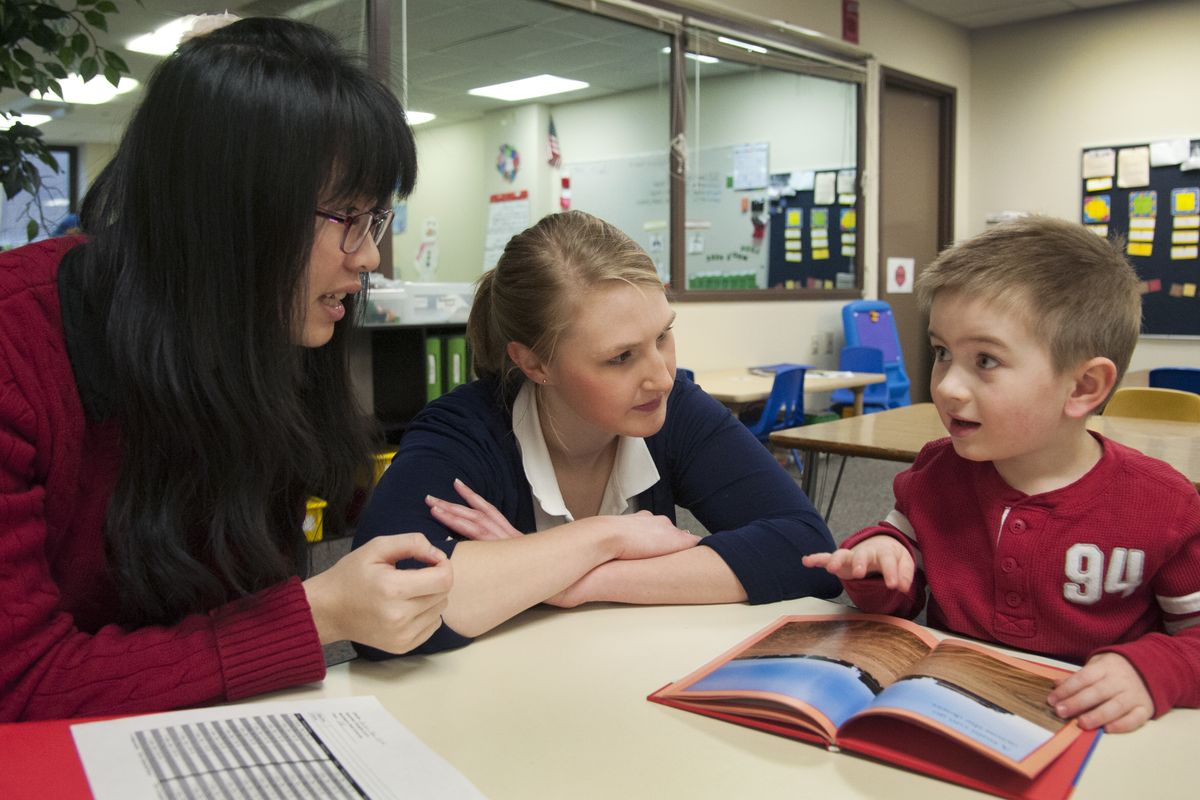 Graduate students Ming-Yeh Hsieh, left, and Lauren Burrows, share a book with Daylon Just, 3, during a session as part of the Domino Project on Jan. 23 in Cheney. (Dan Pelle)