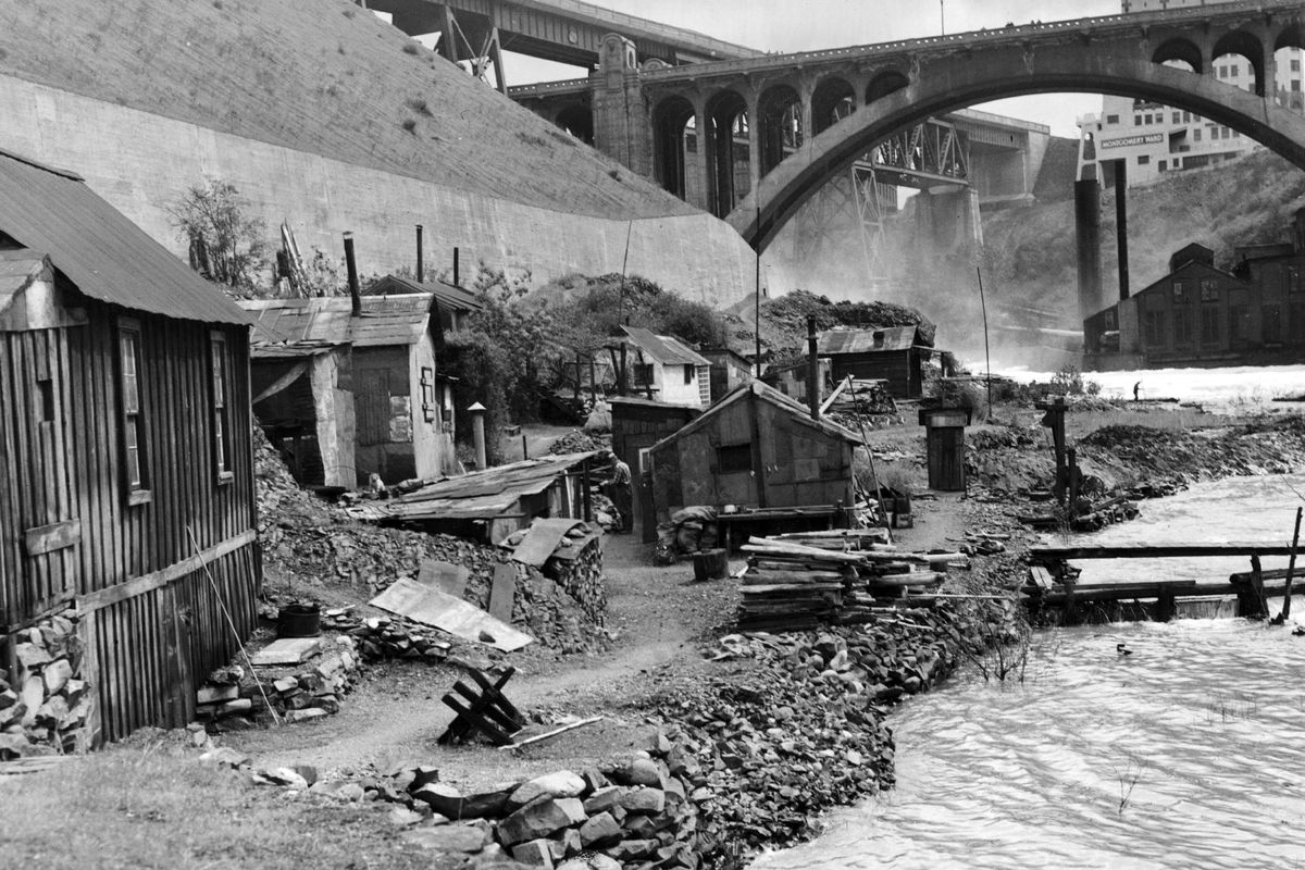 June 7, 1945: This view of “Shacktown” looks east toward the Spokane Falls. When this photo was taken, 20 men lived in the shacks on the banks of the river, near the Monroe Street Bridge. The pier-like structure in the river was there to catch stray wood that would come down from the falls. The wood was dried and used for fires in the winter.